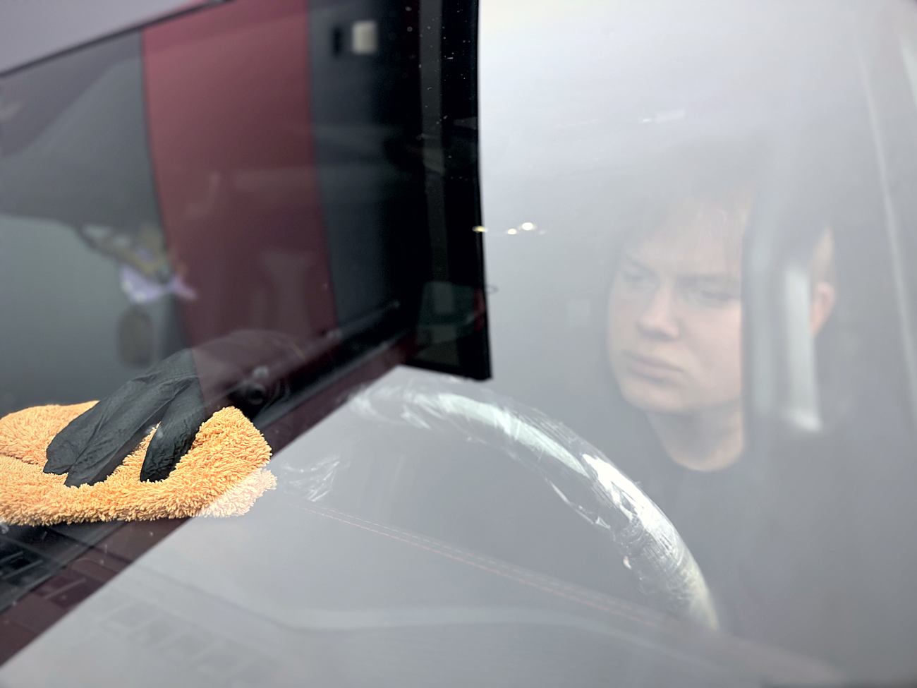 Dłoń w rękawiczce czyści szybę auta z zabezpieczoną kierownicą
