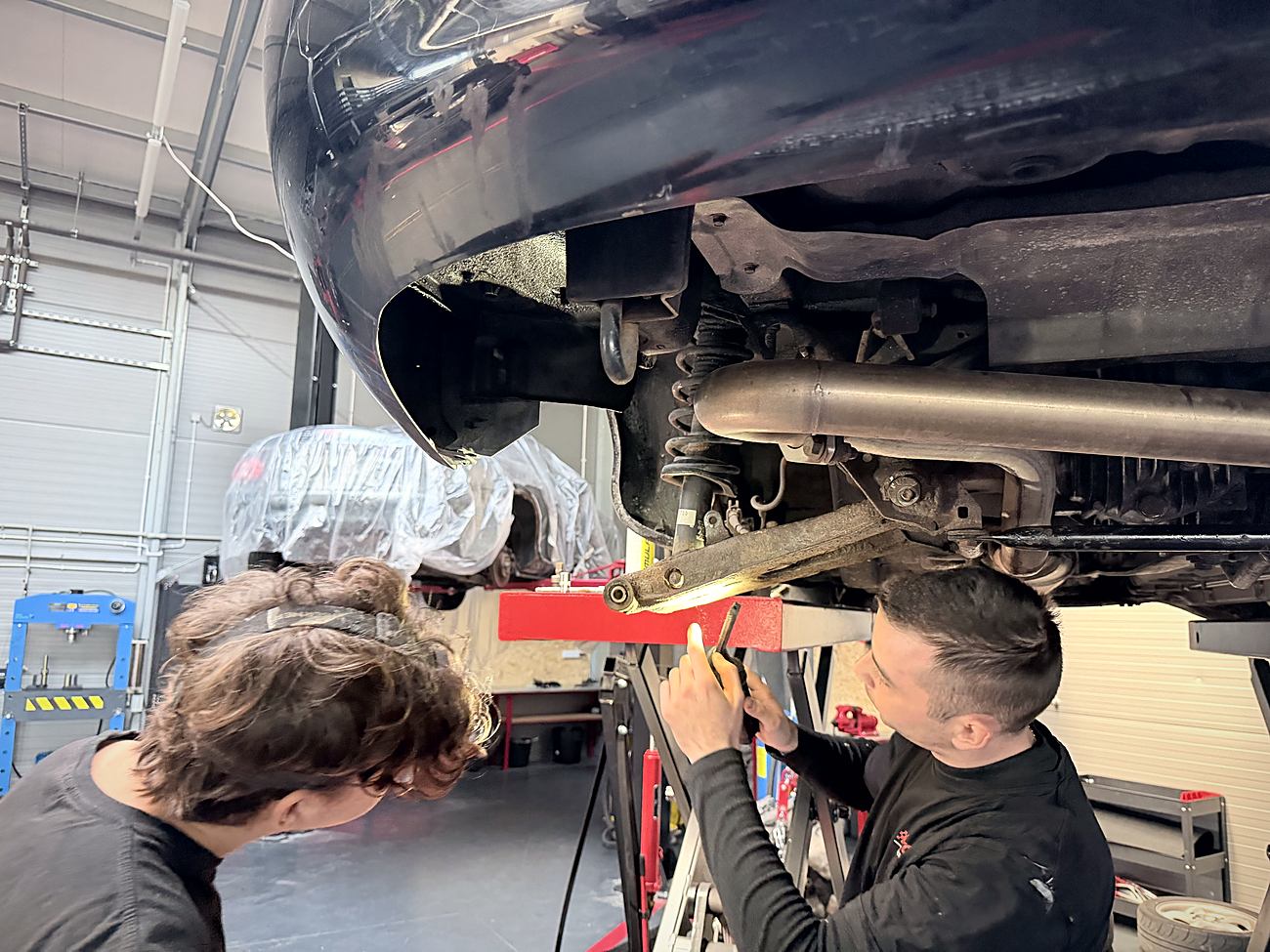 Dwóch mechaników JKN Motors wspólnie pracuje przy zawieszeniu podniesionego auta